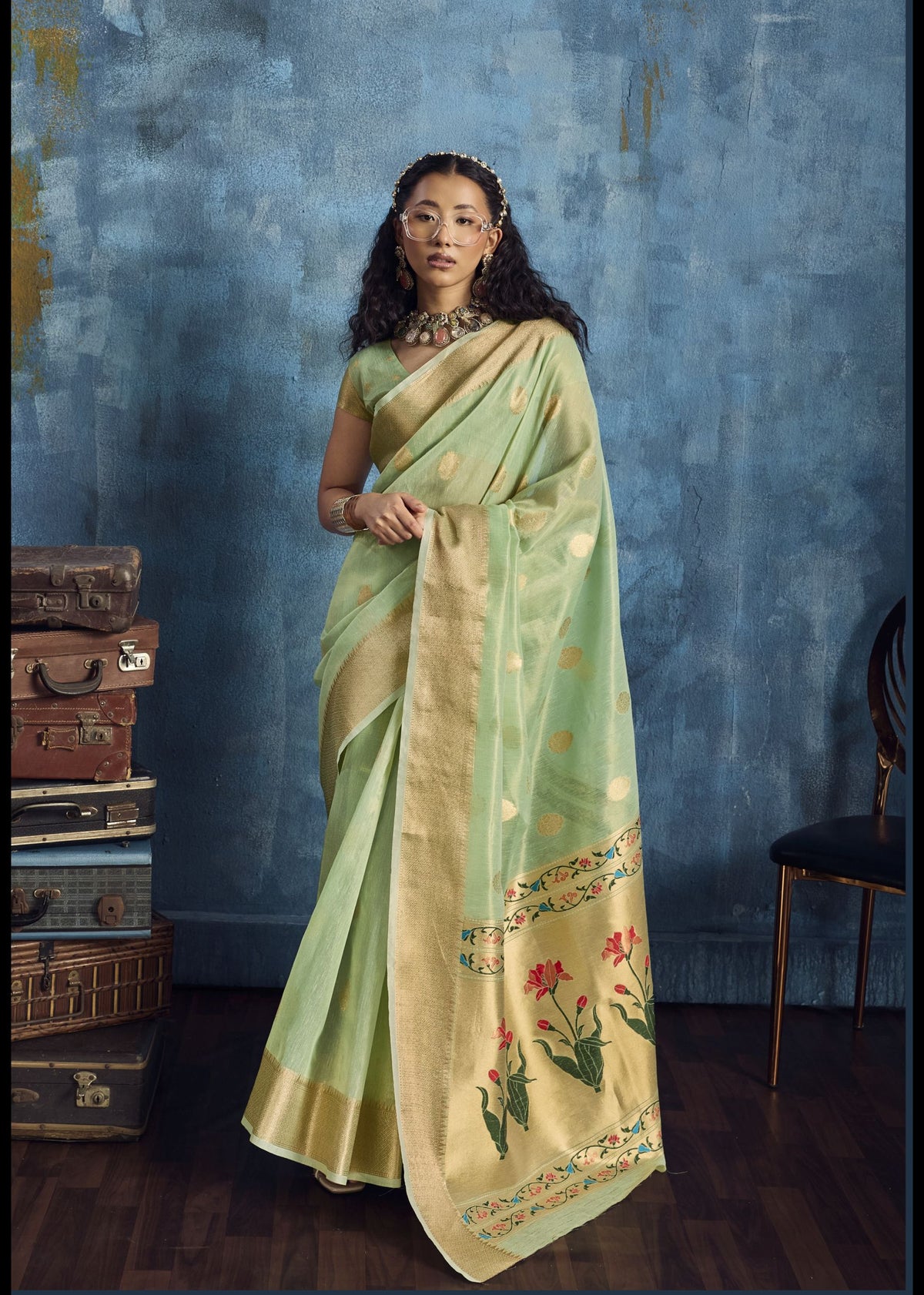Woman wearing a light green saree with floral patterns against a blue textured wall.