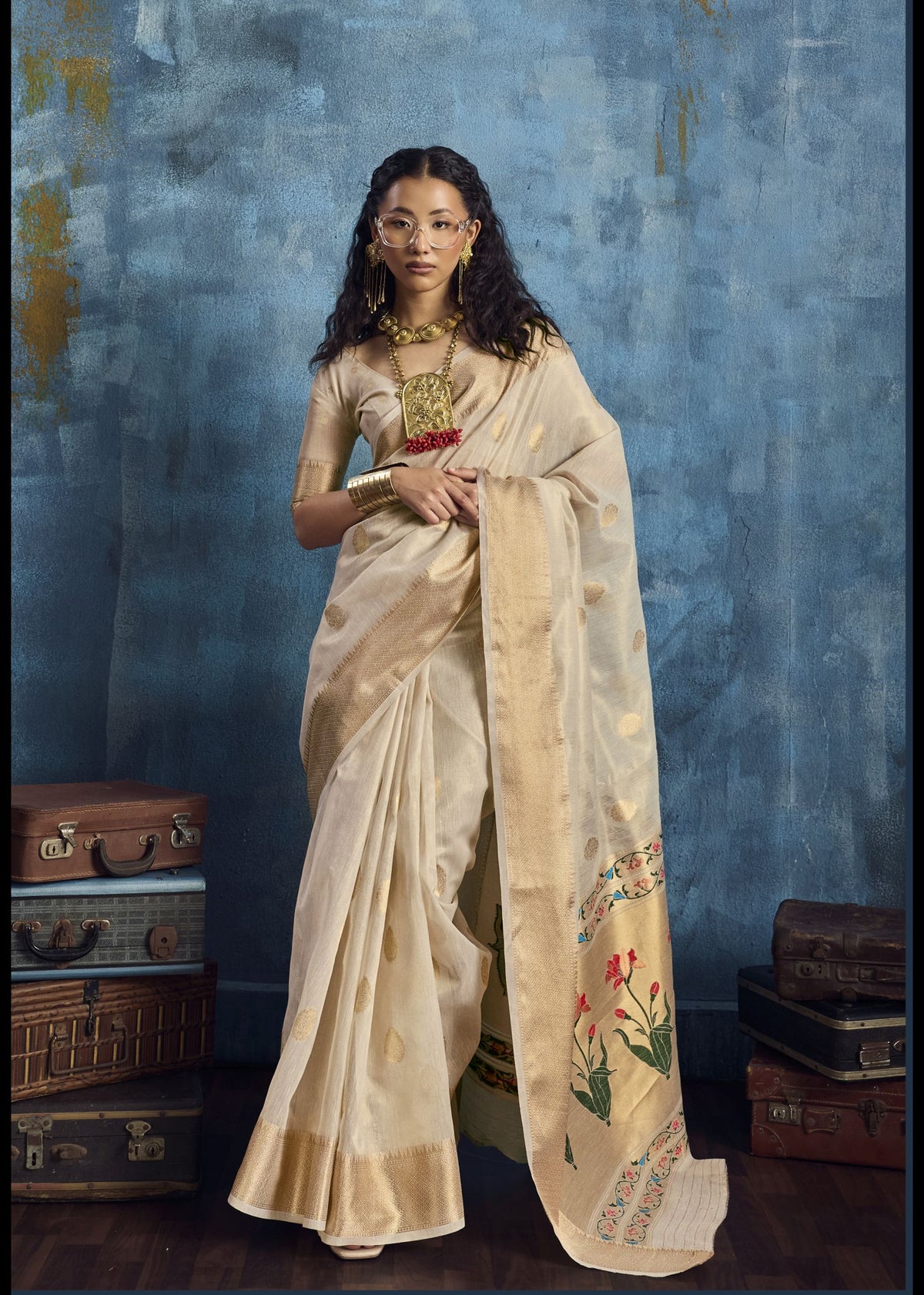 Woman in a traditional saree standing against a textured blue wall with vintage suitcases.