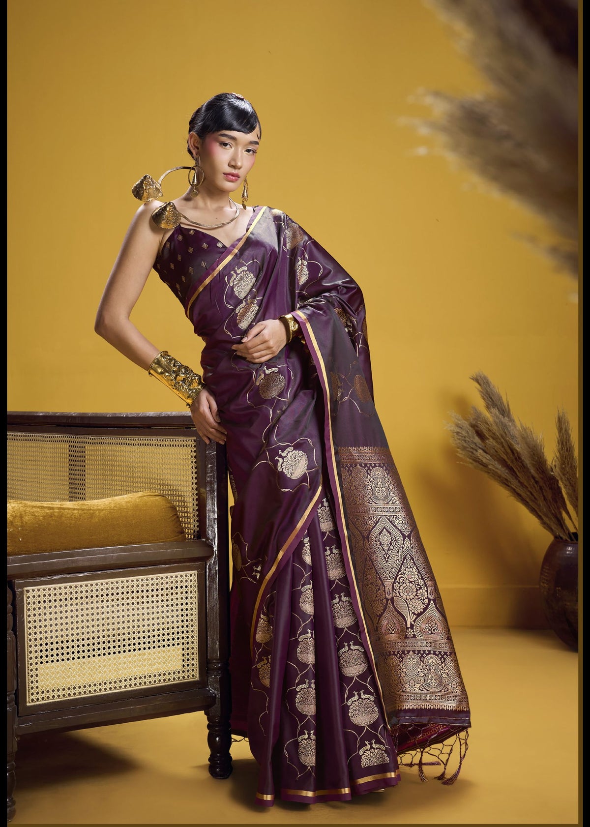 Deep purple silk saree with golden paisley motifs and embellished border.