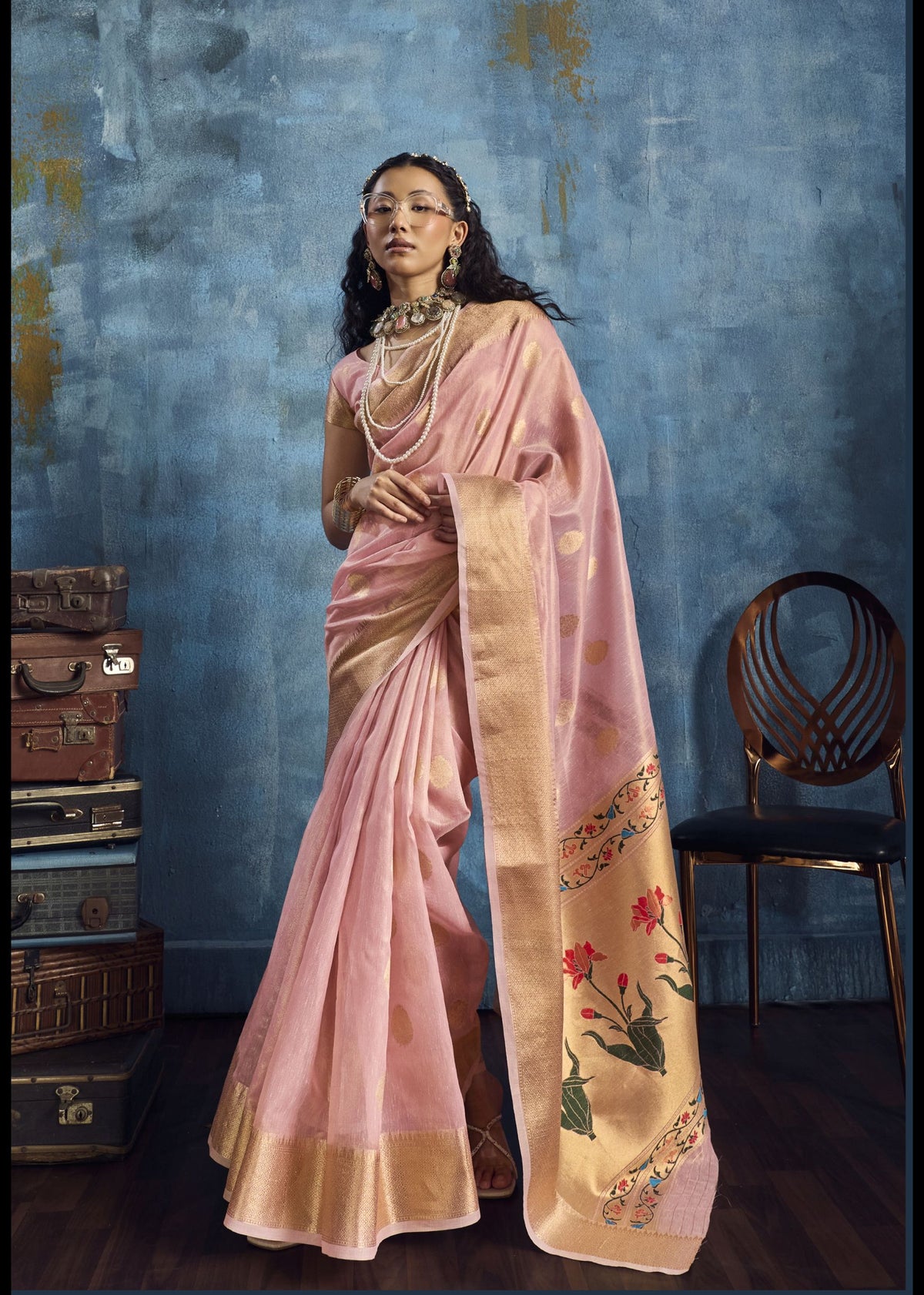 Woman in a pink saree with floral patterns against a textured blue wall.
