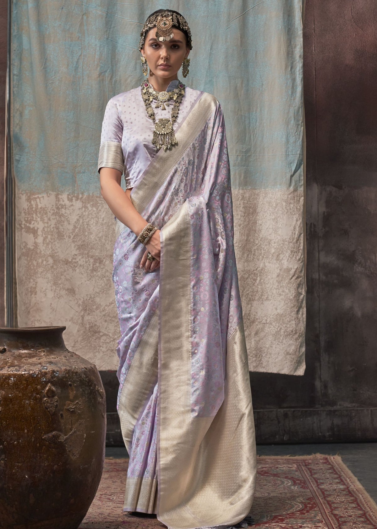 Lavender pure satin handloom saree with intricate floral weaving and a broad silver zari border, paired with a matching satin blouse.