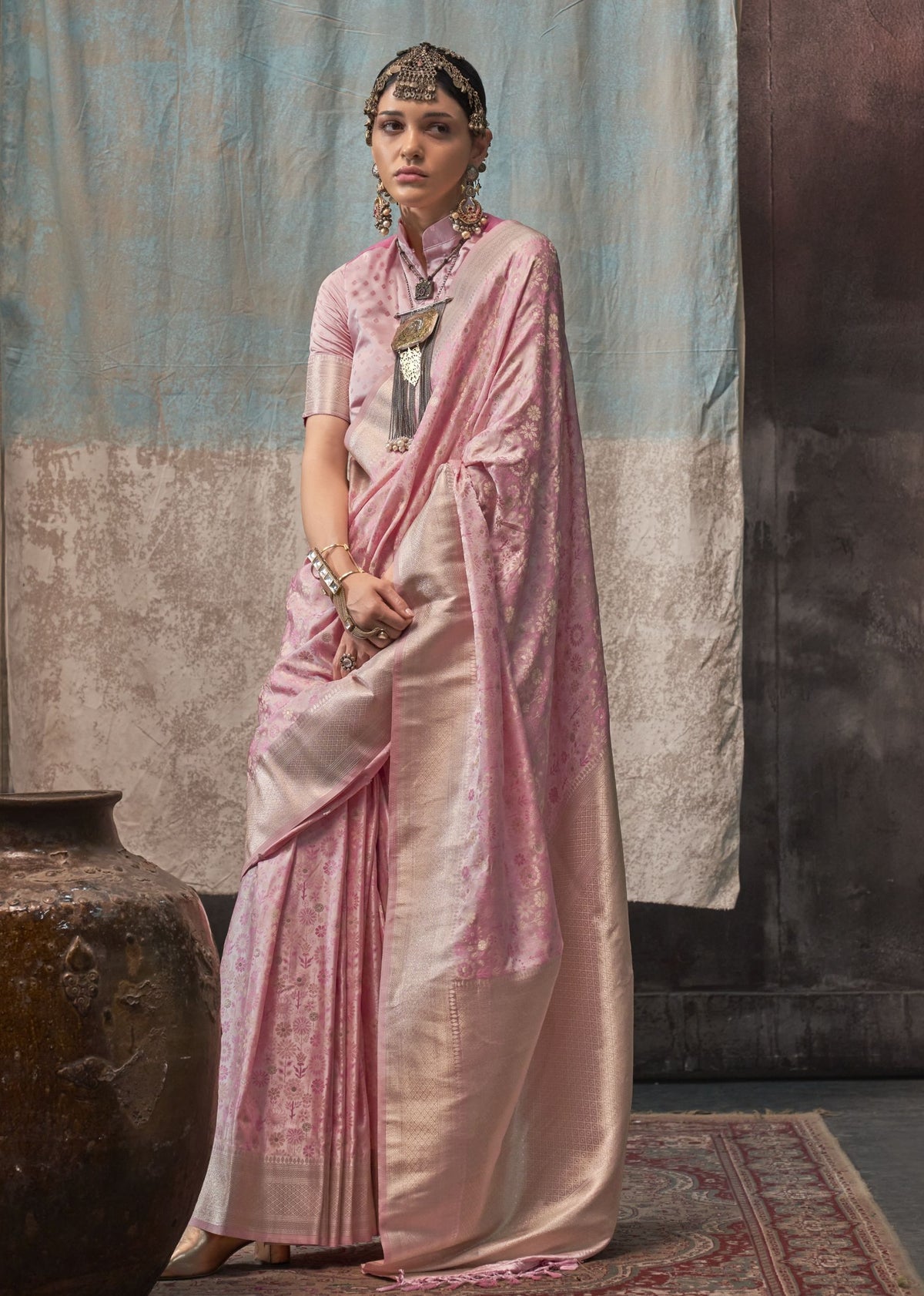 Pink satin saree with a lustrous finish and floral jacquard detailing, paired with a matching high‑neck short‑sleeved blouse.
