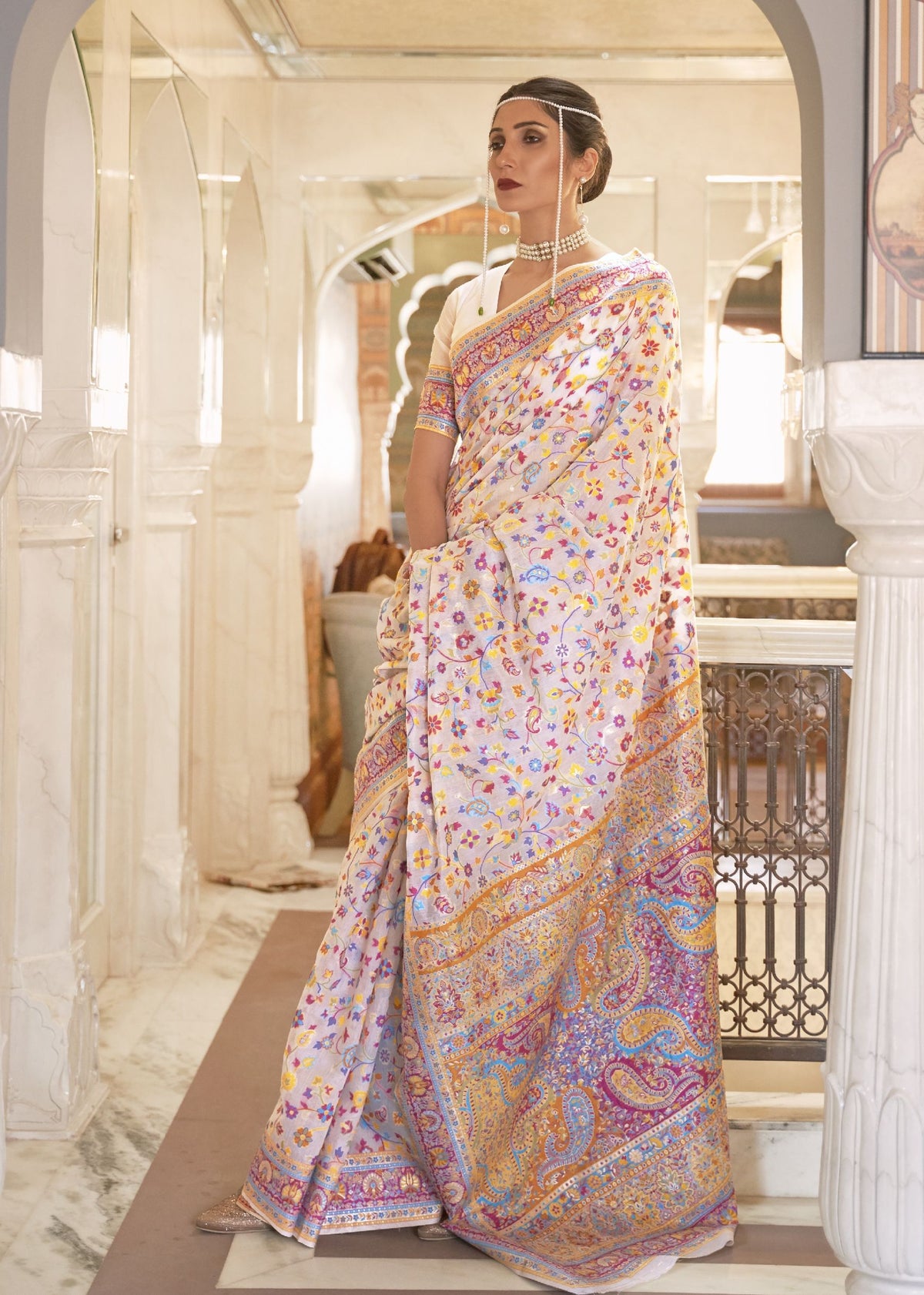 Cream Kashmiri silk saree with multicolored floral and paisley embroidery, styled with pearl jewelry for Indian wedding photography.