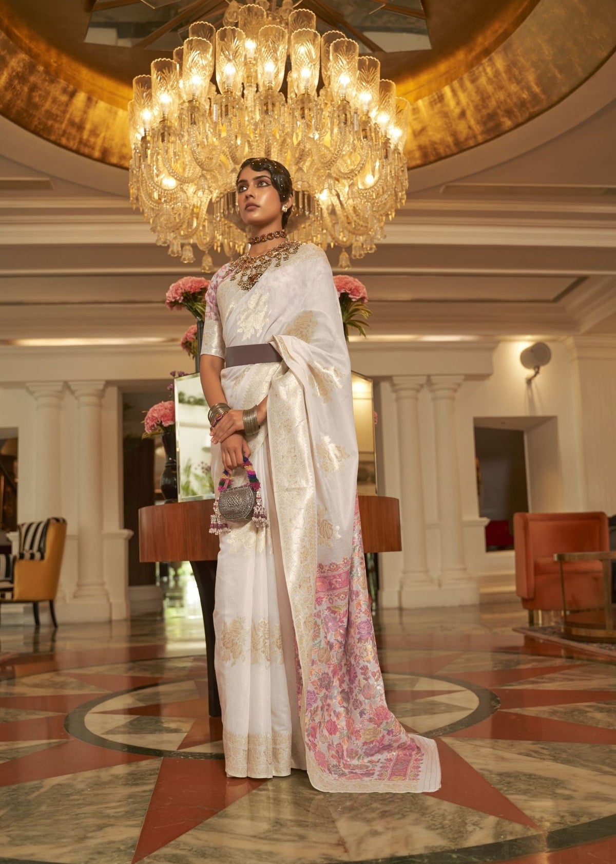White silk saree with gold and blush‑pink floral embroidery and a refined designer finish.