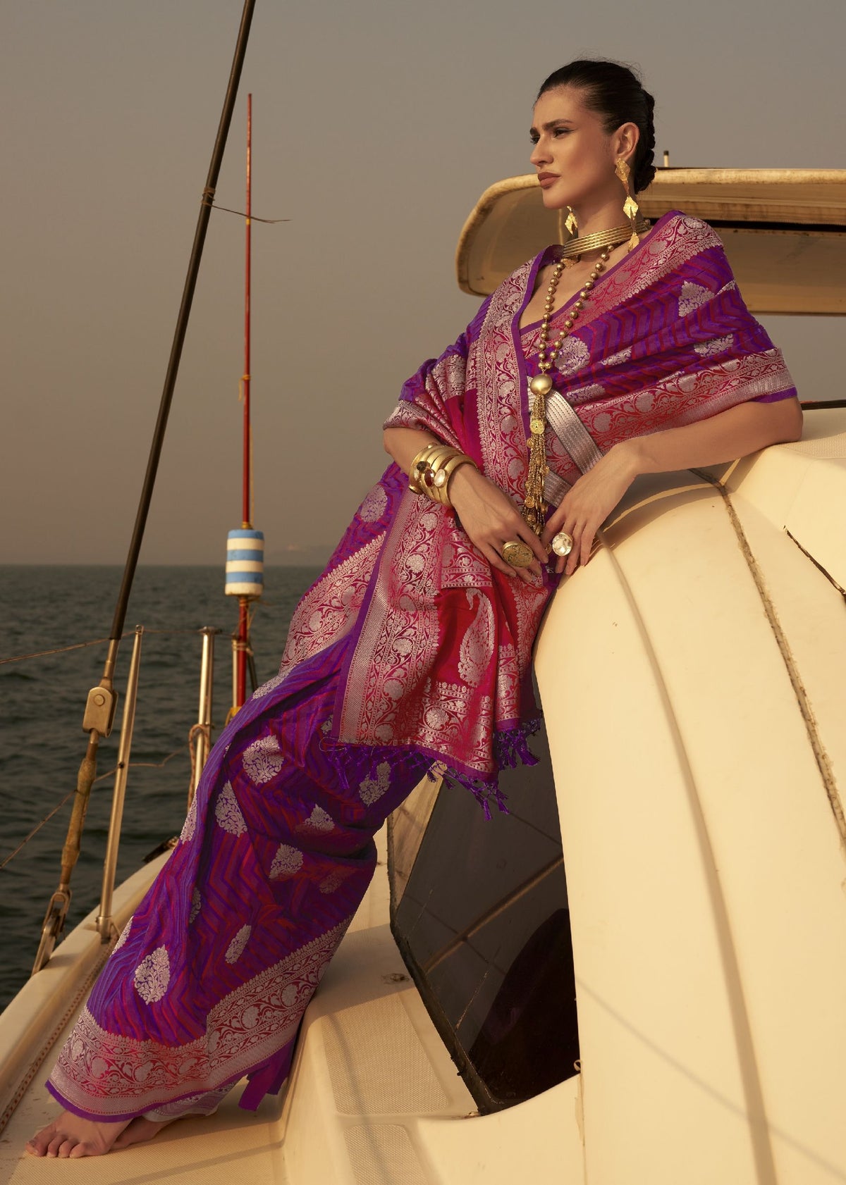 “Purple saree with silver and pink woven embroidery and traditional jewellery accents.”
