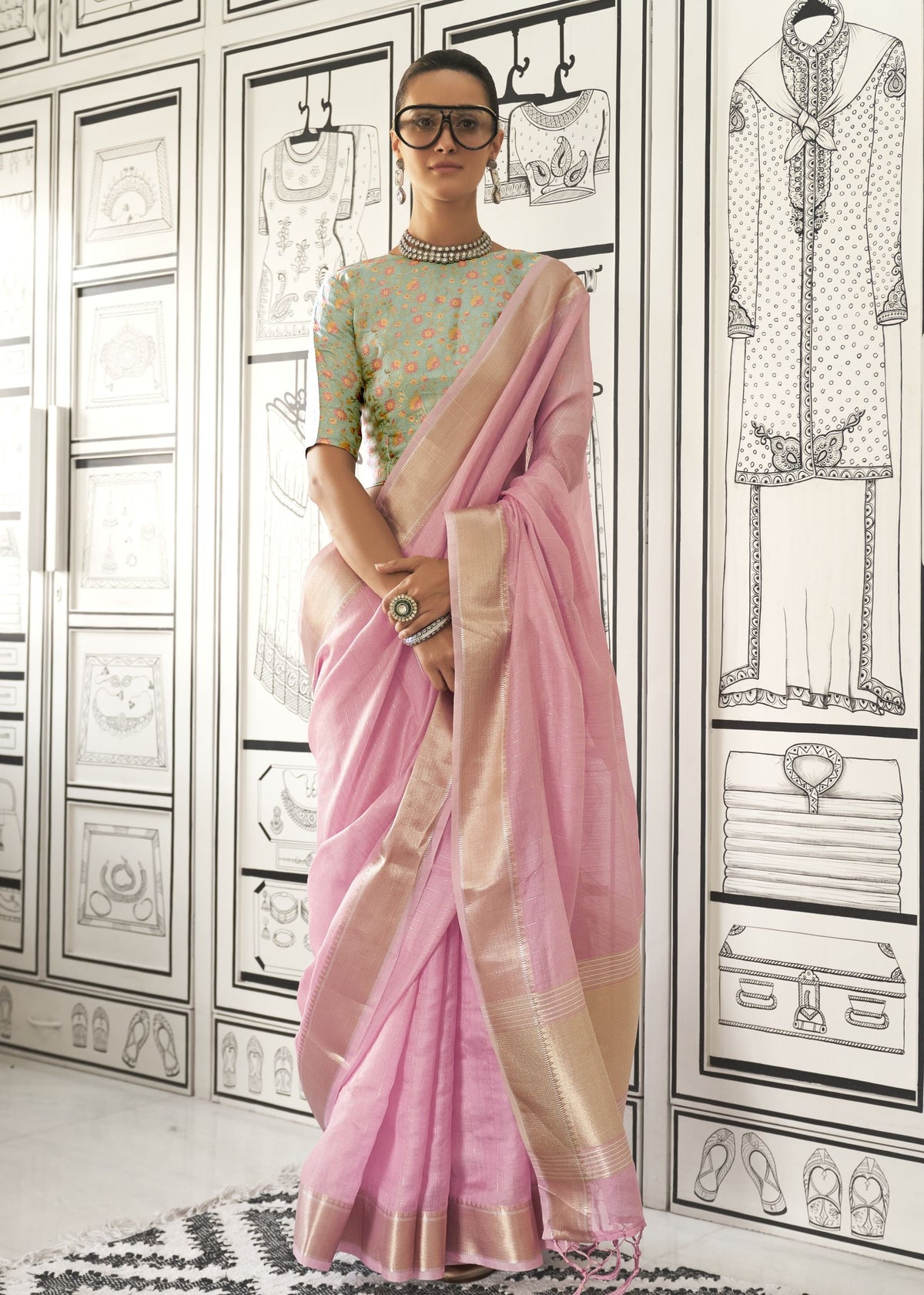 Pastel pink moss chiffon handloom saree with gold border, styled with a blue floral embroidered blouse and statement accessories